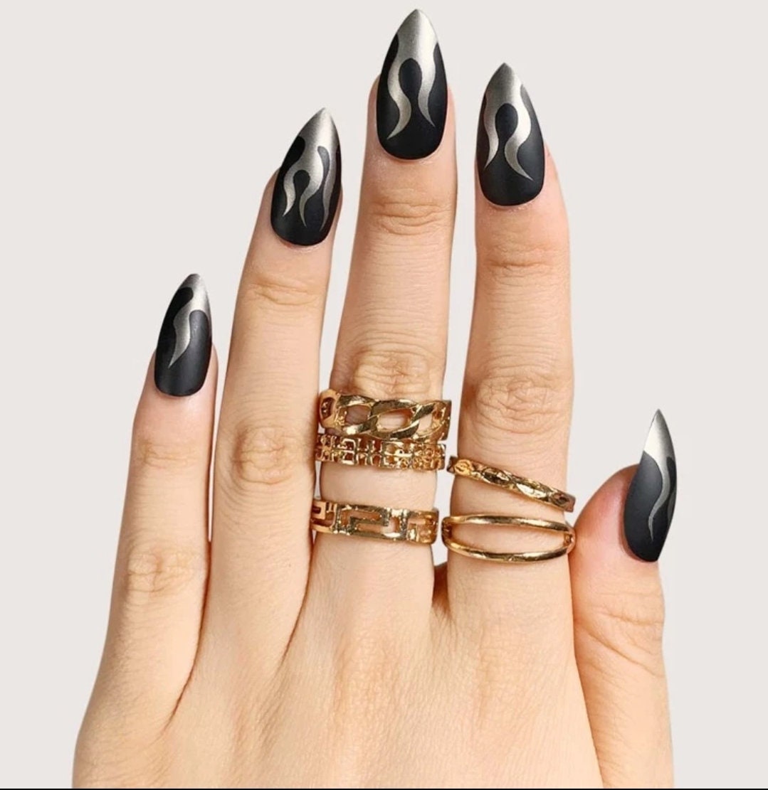 A close-up of a hand with glossy black almond nails wearing silver rings.